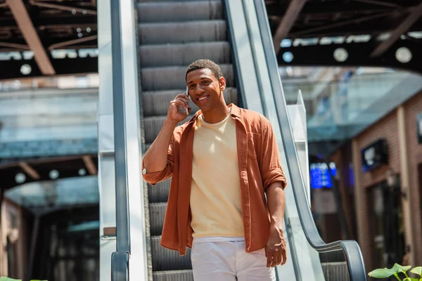 Happy african american man talking on smartphone near escalator — Stock Photo