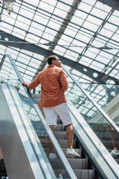 Jovem afro-americano em shorts olhando para longe na escada rolante — Fotografia de Stock