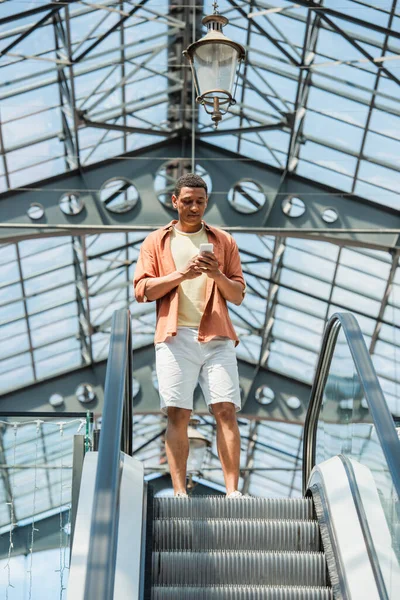 Niedrigwinkel-Ansicht eines afrikanisch-amerikanischen Mannes mit Handy auf Rolltreppe — Stockfoto