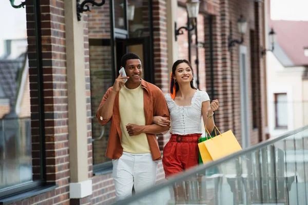 Africano americano homem falando no celular durante a caminhada com asiático namorada — Fotografia de Stock