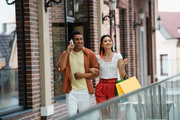 Afro-américain homme parler sur téléphone mobile pendant la promenade avec asiatique copine — Photo de stock