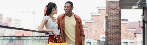 Glücklich afrikanisch-amerikanischer Mann sieht hübsche asiatische Frau mit Einkaufstasche, Banner — Stockfoto