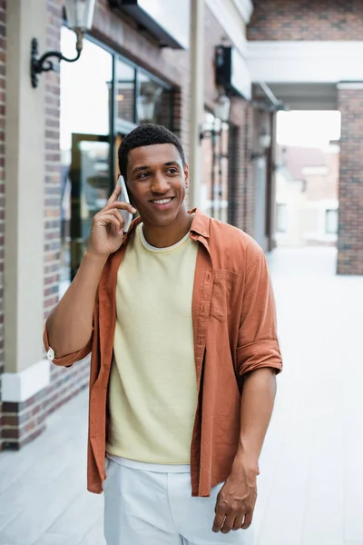 Jeune homme afro-américain souriant tout en parlant sur un téléphone portable dans la rue — Photo de stock