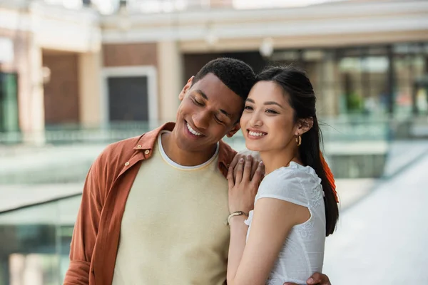 Glücklicher afrikanisch-amerikanischer Mann mit geschlossenen Augen bei lächelnder asiatischer Frau — Stockfoto