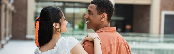 Joven interracial pareja sonriendo el uno al otro al aire libre, bandera - foto de stock