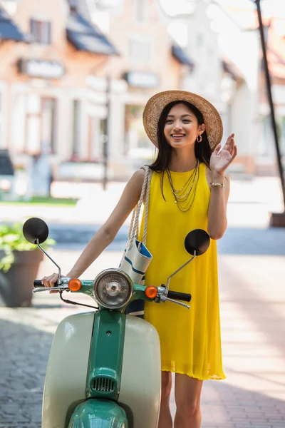 Élégant asiatique femme agitant la main près de scooter à l'extérieur — Photo de stock