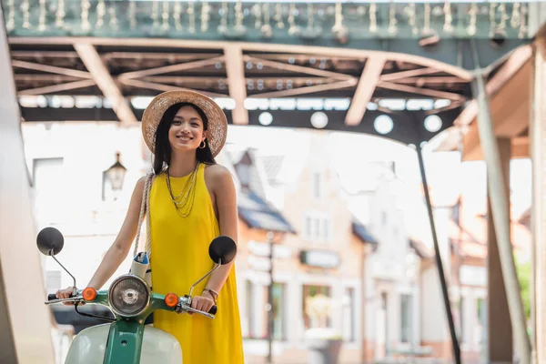 Feliz asiático mujer en amarillo sundress y paja sombrero sonriendo cerca scooter — Stock Photo