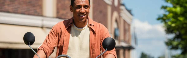 Jovem homem americano africano olhando para longe, enquanto montando scooter ao ar livre, banner — Fotografia de Stock