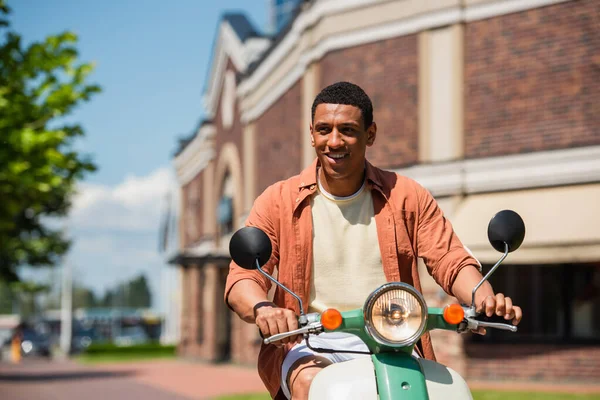 Heureux homme afro-américain souriant tout en équitation scooter en ville — Photo de stock