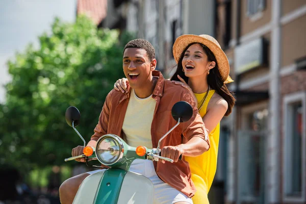 Asombrada pareja multiétnica montando scooter en la calle urbana - foto de stock