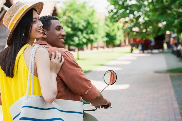 Cheerful asian woman riding scooter with smiling african american man — Stock Photo