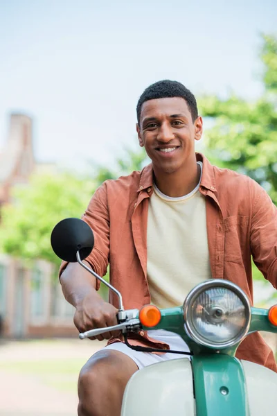 Позитивний афроамериканський чоловік на скутері посміхається на камеру на відкритому повітрі — стокове фото