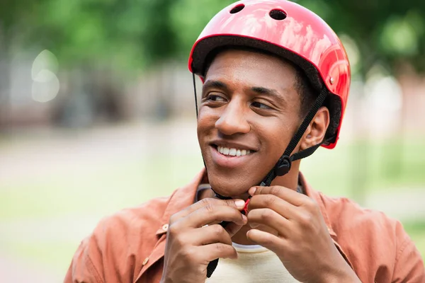 Feliz homem americano africano fixando capacete ao ar livre — Fotografia de Stock