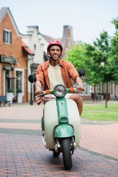 Smiling african american man in helmet enjoying riding scooter in city — Stock Photo