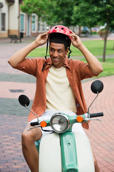 Homme afro-américain positif portant un casque tout en étant assis sur scooter — Photo de stock