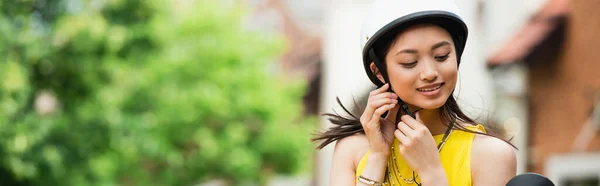 Young asian woman fastening helmet outdoors, banner — Stock Photo