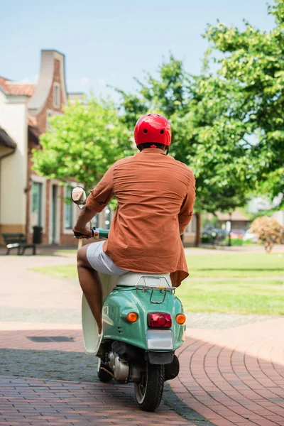 Back view of african american man in hardhat riding scooter in city — Stock Photo