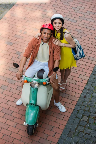 High angle view of stylish asian woman and african american man on scooter smiling at camera — Stock Photo