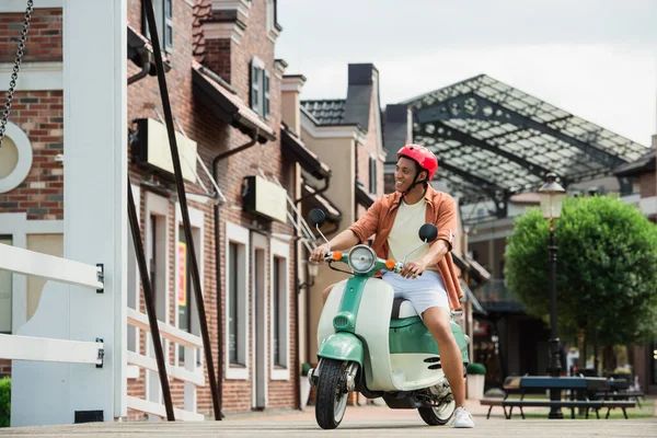 Joven afroamericano hombre en scooter cerca de edificios en la calle urbana — Stock Photo