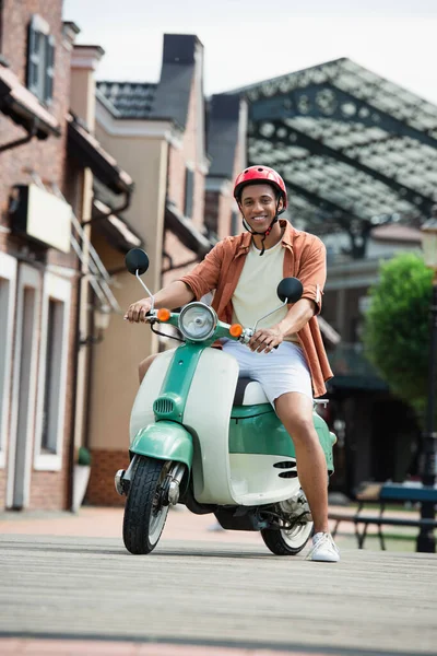 Joven africano americano hombre sonriendo en cámara mientras sentado en scooter — Stock Photo