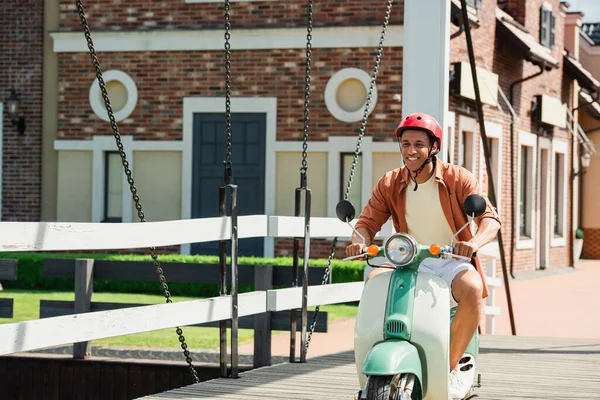 Glücklich afrikanisch-amerikanischer Mann mit Helm fährt Roller auf Brücke — Stockfoto
