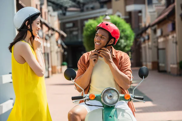 Happy interracial couple looking at each other while fastening hardhats — Stock Photo