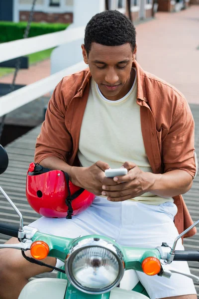 Junger afrikanisch-amerikanischer Mann auf Motorroller sendet Nachrichten auf Handy — Stockfoto