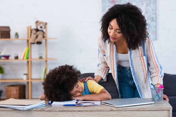 Africano americano mulher olhando para dormir filha perto notebook e laptop — Fotografia de Stock