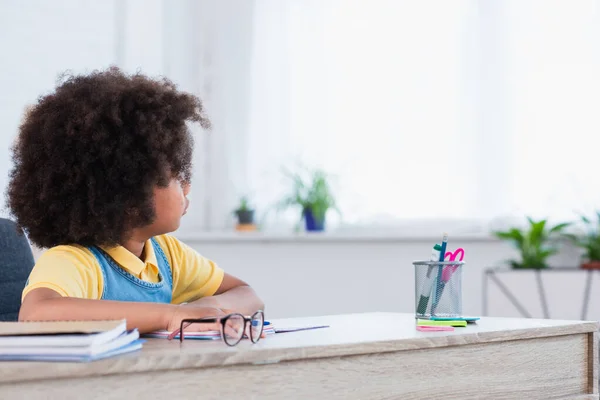 Niño afroamericano mirando hacia otro lado cerca borrosa cuadernos en casa - foto de stock