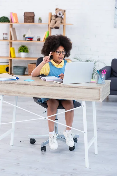 Emocionado niño afroamericano tener idea durante la lección en línea en el ordenador portátil en casa - foto de stock