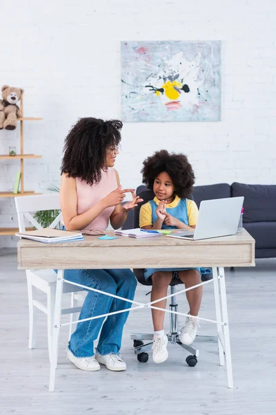 Afroamerikanische Mutter zählt zu Hause an Fingern neben Tochter und Laptop — Stockfoto