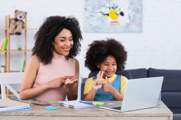 Mère afro-américaine joyeuse et enfant comptant sur les doigts pendant l'apprentissage en ligne sur ordinateur portable à la maison — Photo de stock