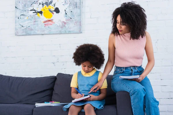 Padres afroamericanos señalando con el dedo mientras el niño escribe en el cuaderno — Stock Photo