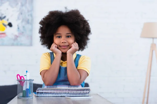 African american kid regardant la caméra près de papeterie et téléphone portable sur la table — Photo de stock