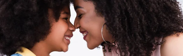 Side view of african american mother and daughter standing nose to nose isolated on white, banner — Stock Photo