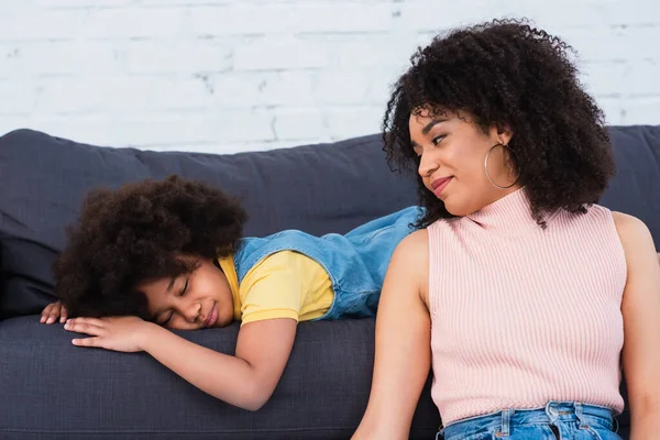 Африканская американская мать смотрит на спящую дочь на диване в гостиной — стоковое фото