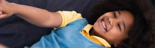 Vista ad alto angolo di sorridente ragazza africana americana sdraiata sul divano, banner — Foto stock