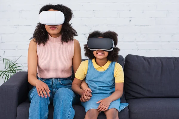 African american family in vr headsets holding hands on couch at home — Stock Photo
