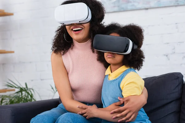 Smiling african american mother hugging daughter in vr headset at home — Stock Photo