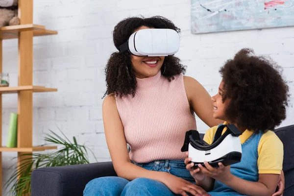 Smiling african american girl holding vr headset near mother gaming at home — Stock Photo