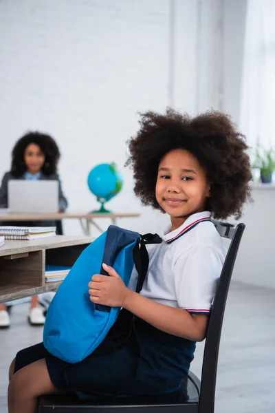 Lächelndes afrikanisches amerikanisches Kind mit Rucksack im Klassenzimmer — Stockfoto