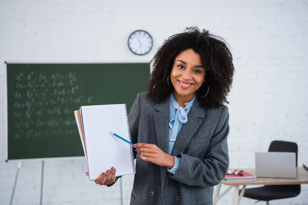 Sorridente insegnante afro-americano che indica il taccuino in classe — Foto stock