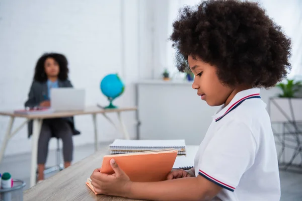 Vista laterale di africano americano studentessa lettura libro a scuola — Foto stock