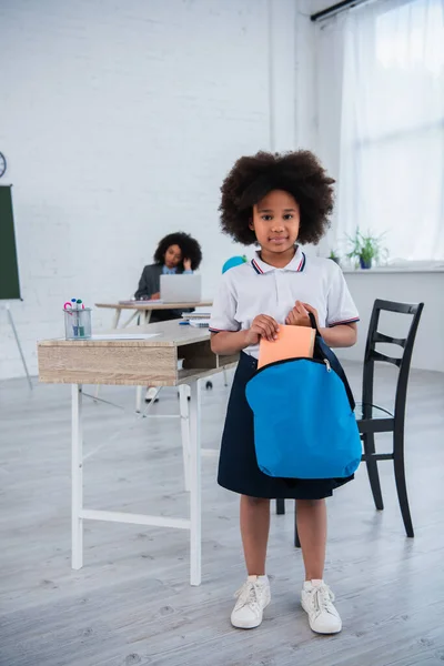 Aluno afro-americano segurando mochila e livro em sala de aula — Fotografia de Stock