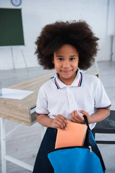 Colegiala afroamericana sosteniendo libro y mochila - foto de stock