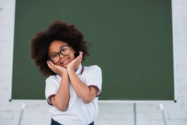 Positivo pupillo afro-americano con gli occhiali che guarda la fotocamera in classe — Foto stock