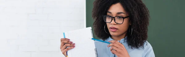 African american teacher pointing at notebook in classroom, banner — Stock Photo