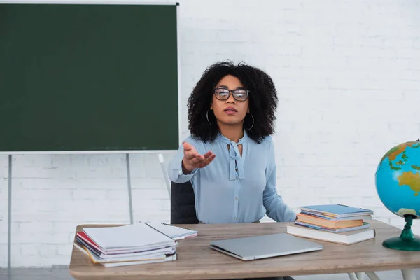 Professeur afro-américain pointant avec la main près d'un ordinateur portable et des ordinateurs portables en classe — Photo de stock