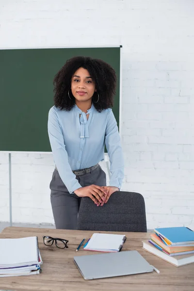 Professor afro-americano em pé perto de laptop e notebooks na mesa — Fotografia de Stock