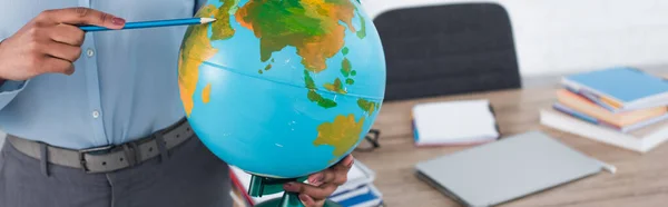 Cropped view of african american teacher pointing with pencil on globe in classroom, banner — Stock Photo